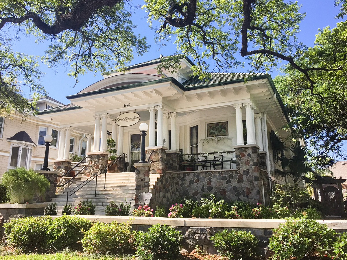 Canal Street Inn exterior with Greek Revival columns, stained-glass window, and blooming gardens